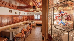 Un restaurant avec des boiseries, une longue table conviviale et un vitrail orné d’un blason.