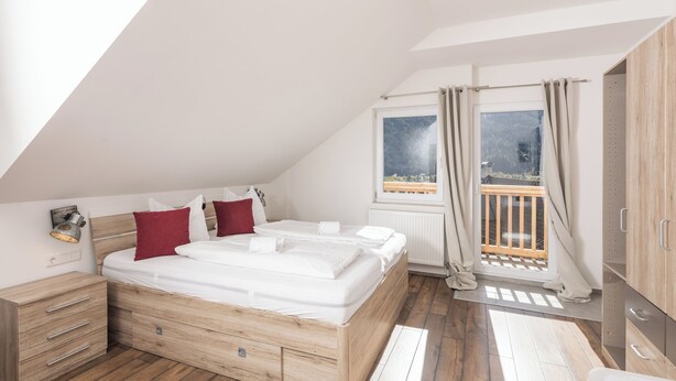 Une chambre à coucher avec un lit en bois, une table de chevet, une fenêtre avec des rideaux et une vue sur un balcon.