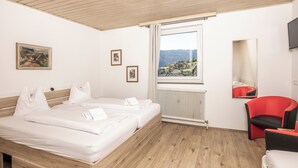 Une chambre à coucher avec un lit en bois, une chaise rouge, une fenêtre donnant sur les montagnes et un radiateur.