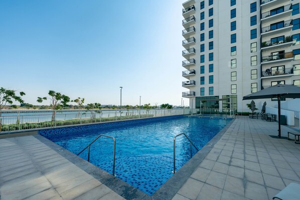 A swimming pool with a tiled deck, surrounded by a high-rise building with balconies. - Charming Retreat w Panoramic Views on Yas Island (Abu Dhabi)