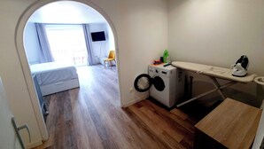 En kompakt lejlighed med vaskefaciliteter, et lille opholdsområde og udsigt gennem en buet åbning til en balkon.