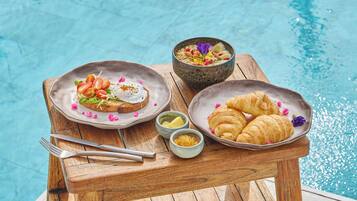 Une table en bois, dressée avec des aliments pour le petit-déjeuner, se trouve au bord de la piscine.