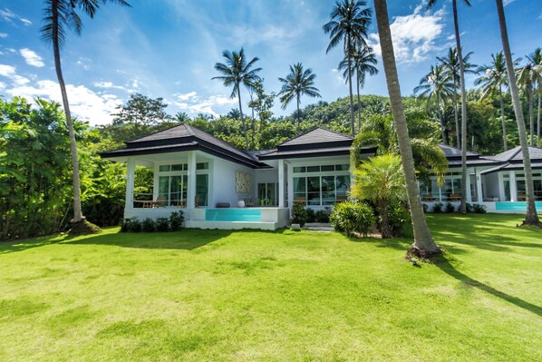 A modern house with a large lawn, surrounded by palm trees and lush greenery.