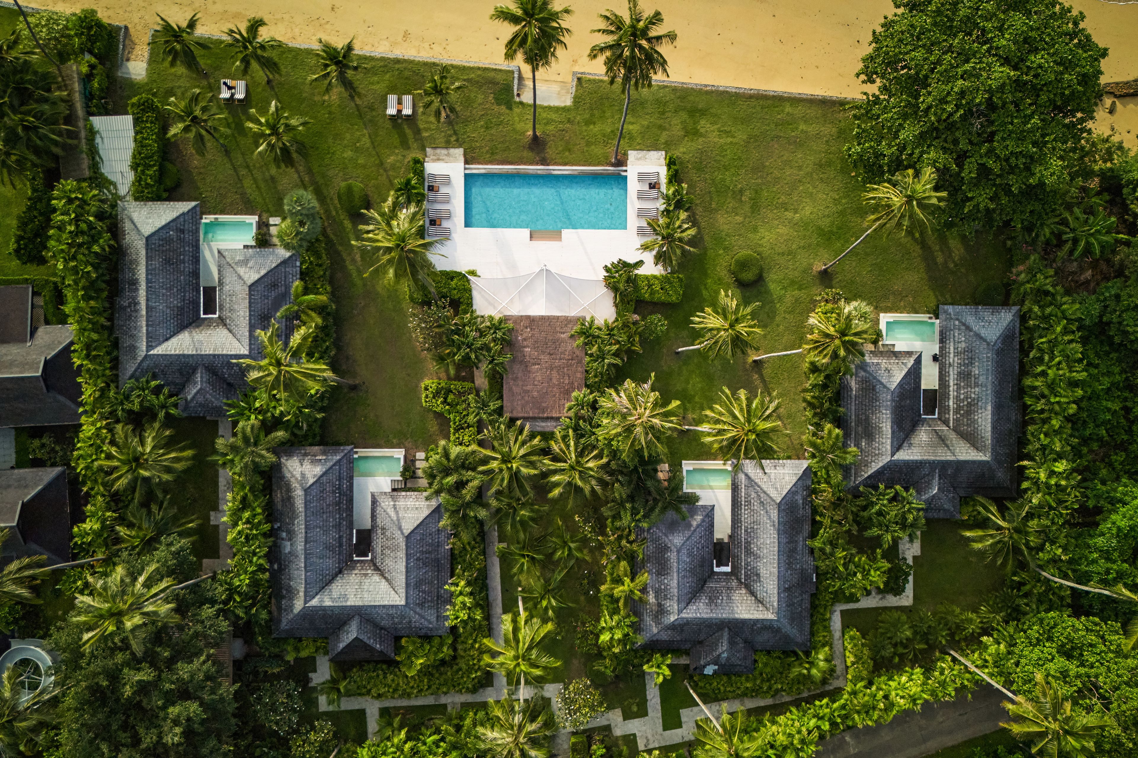 Un complejo turístico con varias cabañas, una piscina central y exuberante jardinería tropical.