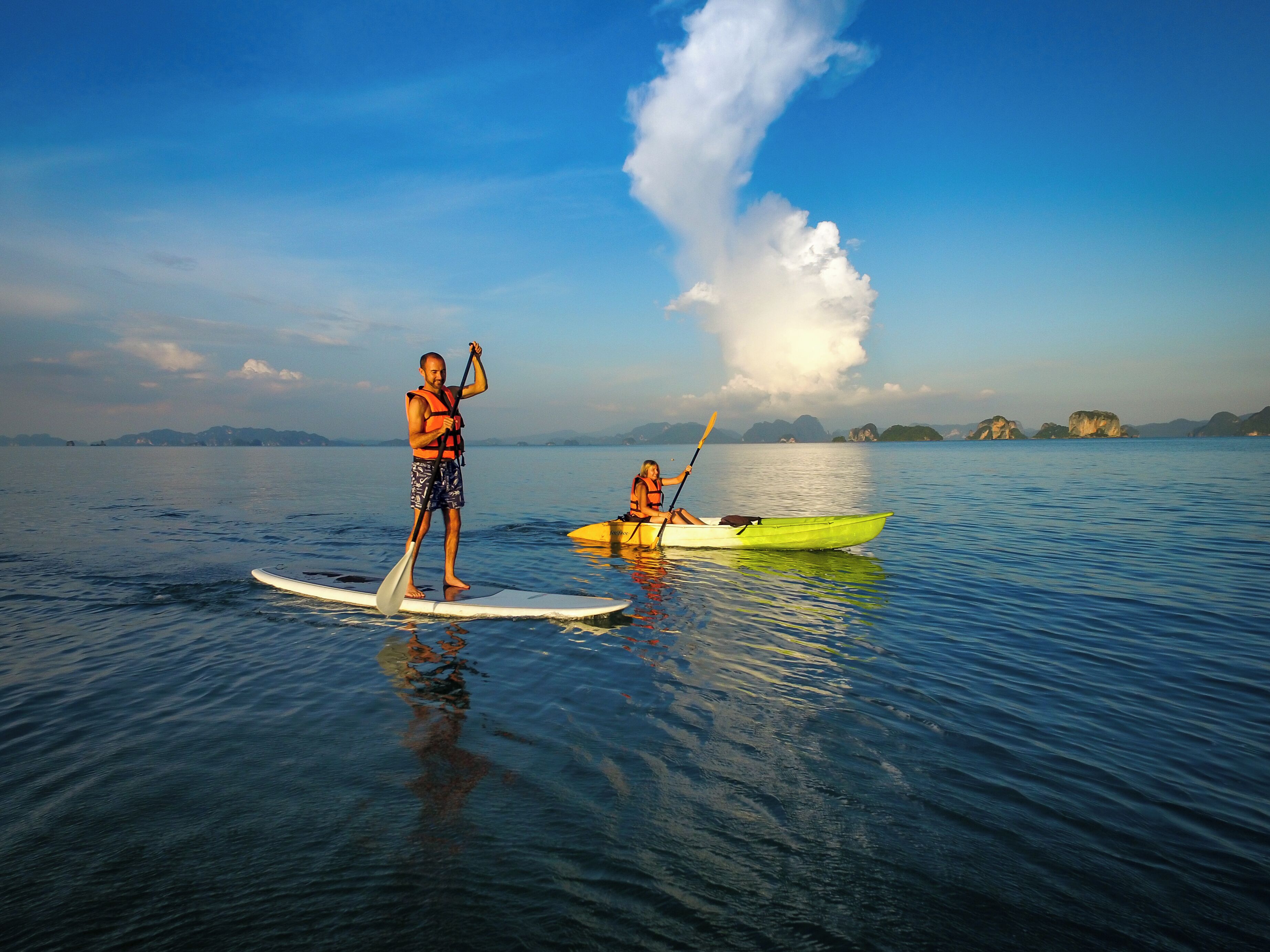 Two people paddleboarding on calm water with a clear sky and distant islands.