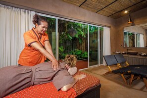 A massage therapy room with a large sliding glass door leading to a garden, a massage table, and a small reception area with a counter and chairs. - Coastal Escape Koh Yao Noi (Ko Yao)
