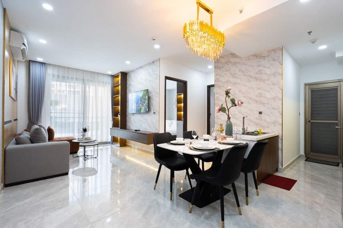 A modern living room with a sofa, dining table, and chairs. There is a chandelier, a TV, and a window with curtains.