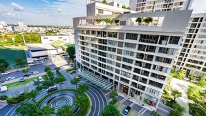 A modern multi-story building with a rooftop garden, a circular driveway, and a parking area.