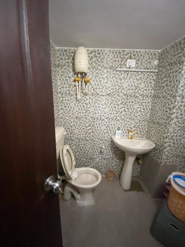 Une salle de bain équipée de toilettes, d’un lavabo et d’un chauffe-eau fixé au mur.
