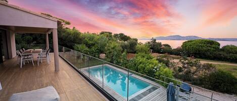 A modern outdoor pool area with a view of the sea and mountains during sunset.