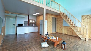 A spacious living area with a wooden staircase, a kitchen with modern appliances, and a dining table set with a bottle and glasses.