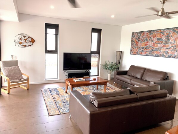 A modern living room with a brown leather sofa, a wooden coffee table, a TV, and a decorative wall piece.