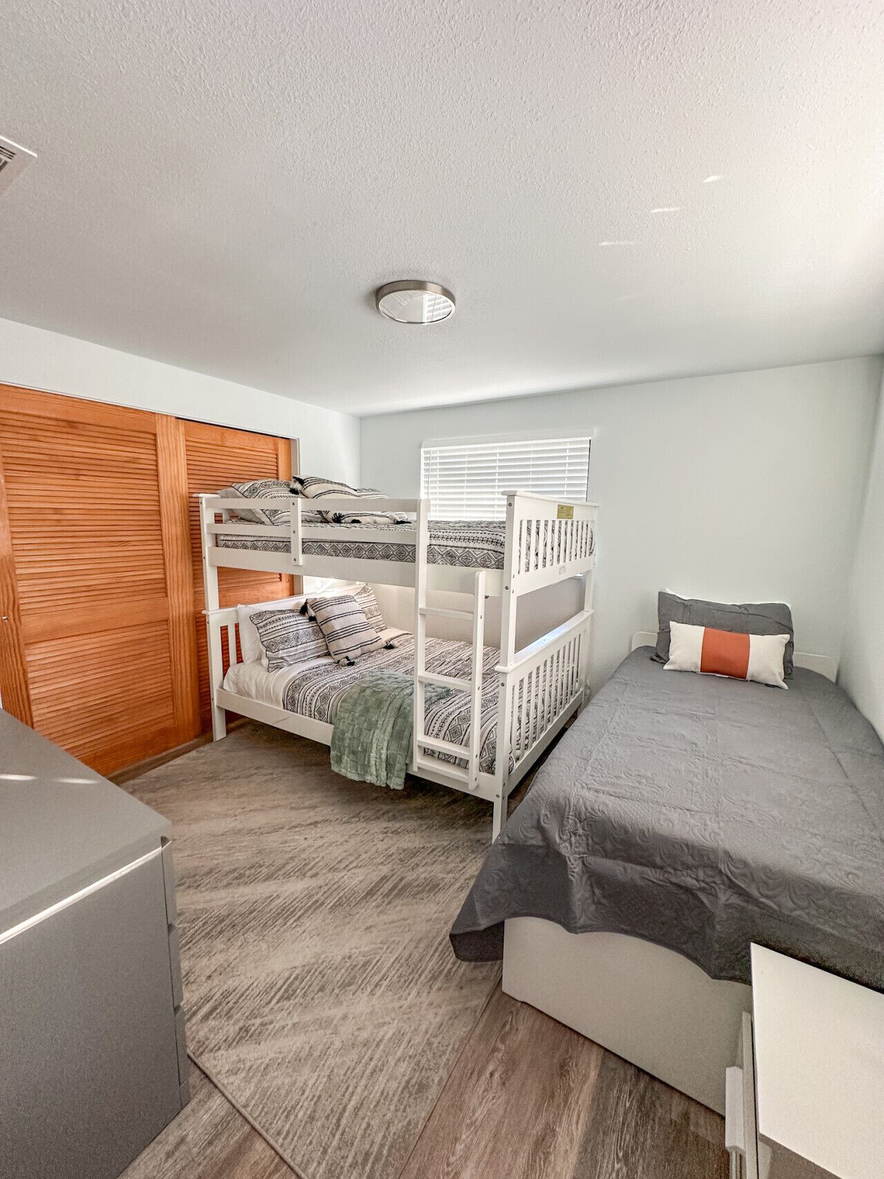 A bedroom with a bunk bed, a single bed, a wooden wardrobe, and a small desk.