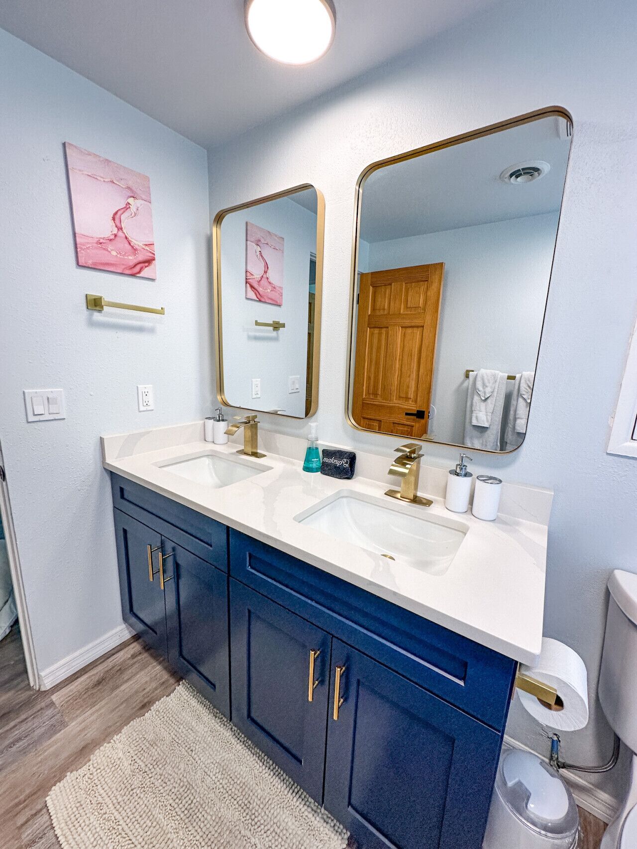 Une salle de bain avec deux lavabos, un grand miroir, une porte en bois et un porte-serviettes.