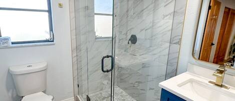 Un baño moderno con ducha de vidrio, inodoro y tocador con espejo.