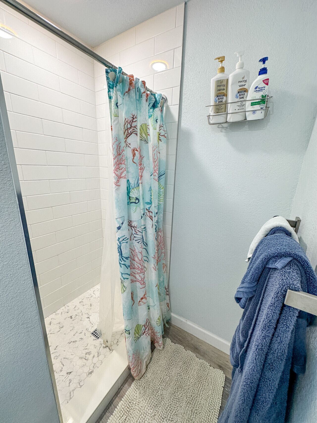 A shower with a colorful curtain, a towel rack with a blue towel, and toiletries on a shelf.