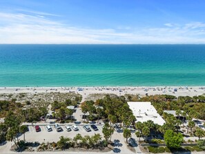 Ein Strand mit Parkplatz und Gebäuden im Vordergrund.