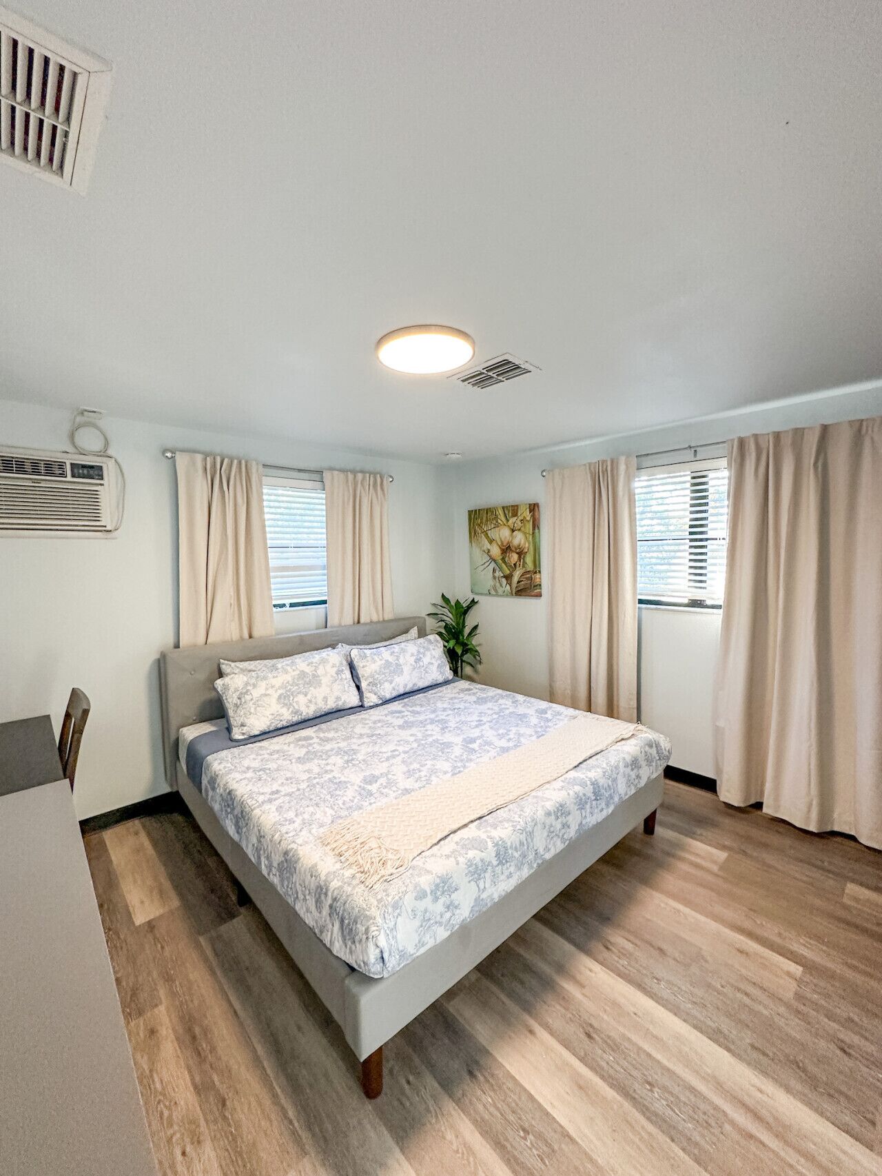 A bedroom with a bed, curtains, a ceiling light, an air conditioning unit, and a window.