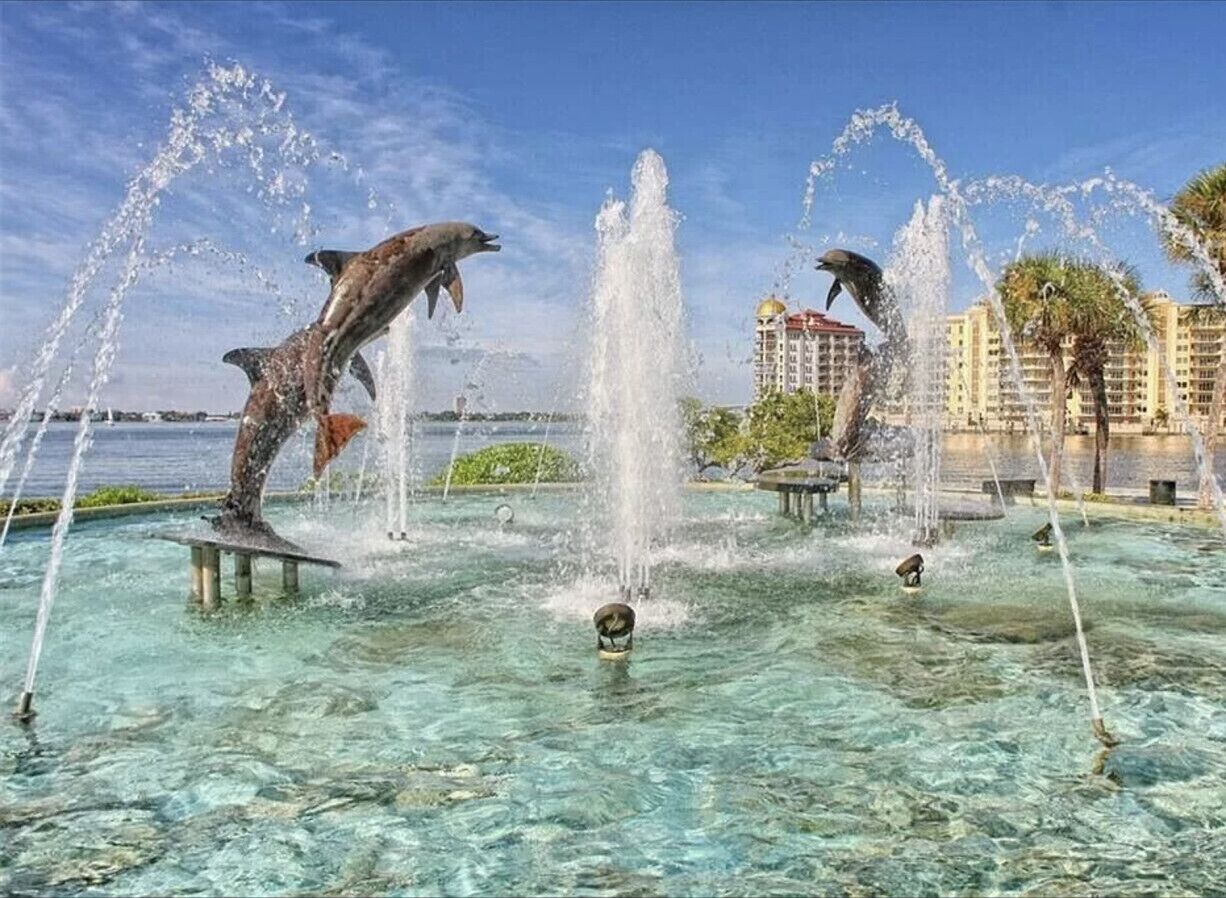 Une fontaine ornée de sculptures de dauphins, située dans un espace où l’eau est claire et entourée de bâtiments.