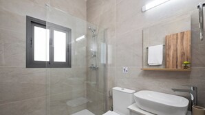 Une salle de bain moderne avec une douche à parois de verre, des toilettes blanches et un lavabo avec un meuble-vasque en bois.
