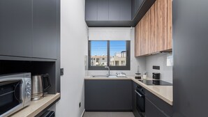 Une cuisine moderne avec des meubles gris, un four à micro-ondes en acier inoxydable, un évier et une fenêtre donnant sur des immeubles.