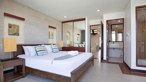 Una cama grande con estructura de madera, una mesita de noche, un espejo y un baño con ducha y lavamanos.