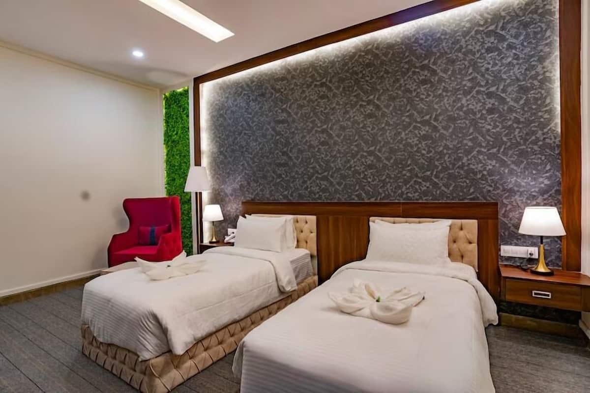 A hotel room with two beds, a red chair, and a green wall.