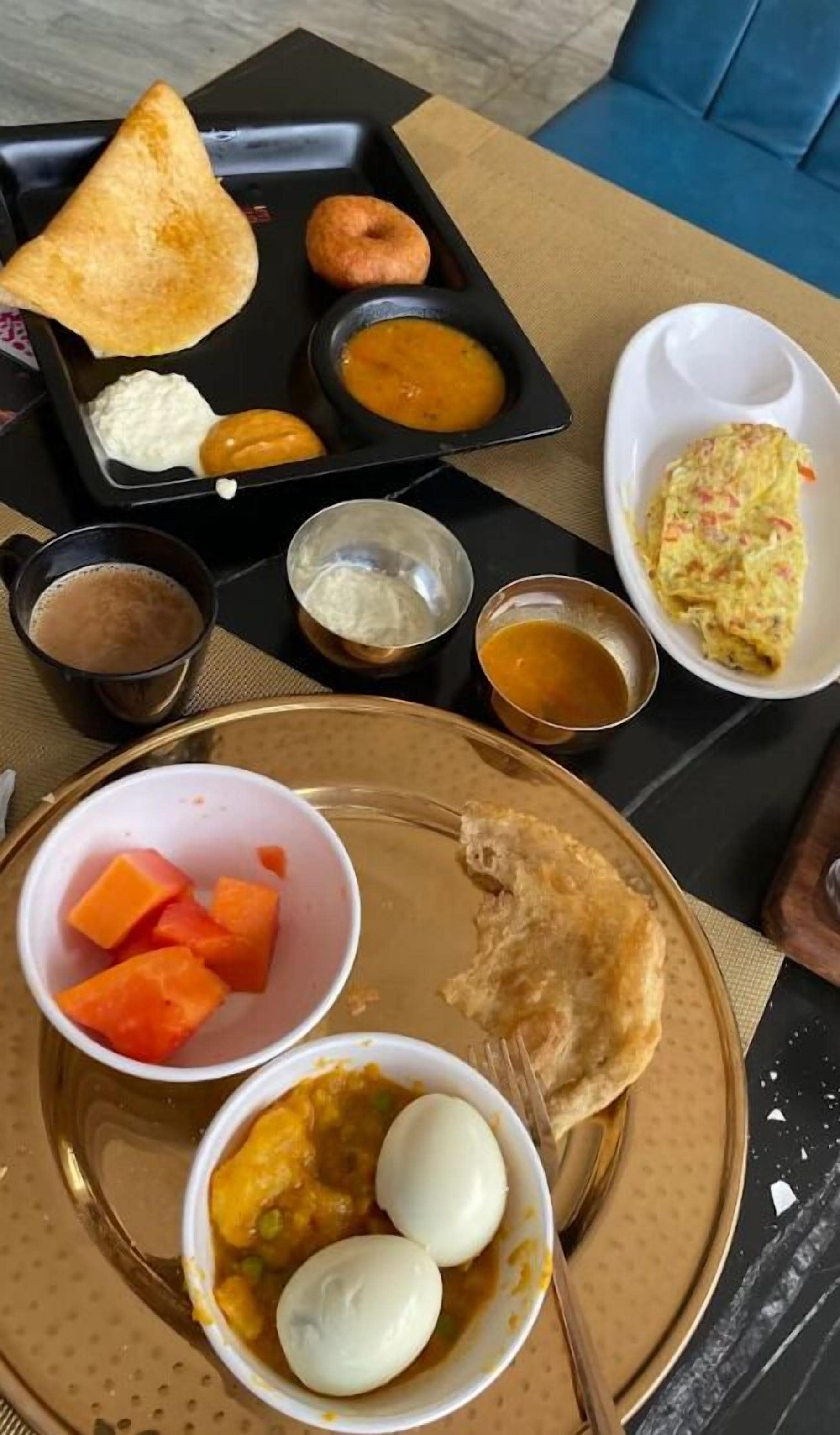 A tray with various food items including a samosa, a fried item, and a plate with eggs and a curry dish.