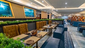 A modern restaurant interior with booth seating and long tables, featuring a green plant wall and a view of the city. - Essotto Recreation Hub (Bengaluru)