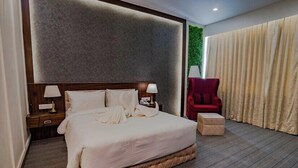 A hotel room with a large bed, a nightstand, a red chair, and a green wall. - Essotto Recreation Hub (Bengaluru)