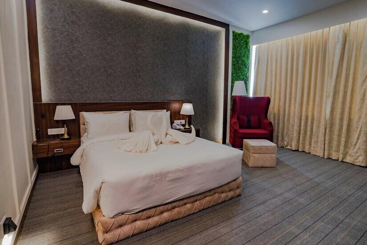 A hotel room with a large bed, a nightstand, a red chair, and a green wall.
