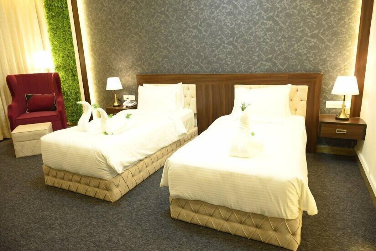 A hotel room with two beds, a red armchair, and a green wall.