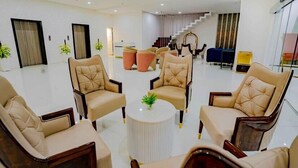 A spacious lobby with a modern design, featuring a seating area with leather chairs and a central coffee table. A staircase is visible in the background leading to an upper floor. - Essotto Recreation Hub (Bengaluru)