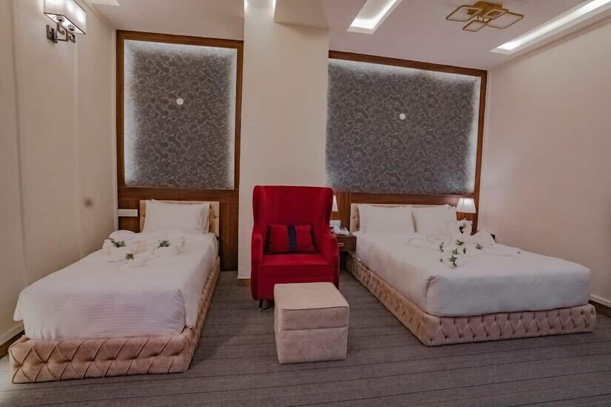 A hotel room with two beds, a red chair, and a small ottoman.