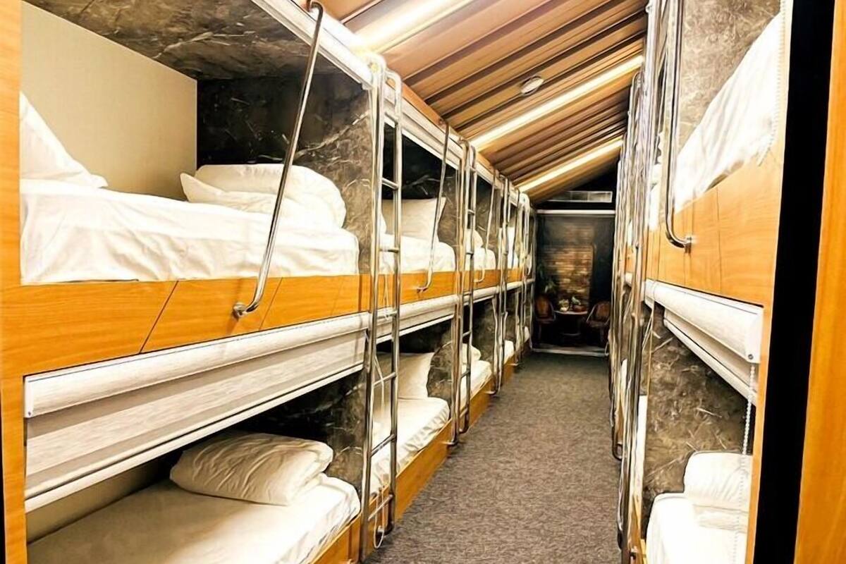 A narrow, enclosed train carriage with wooden bunk beds and a carpeted floor.