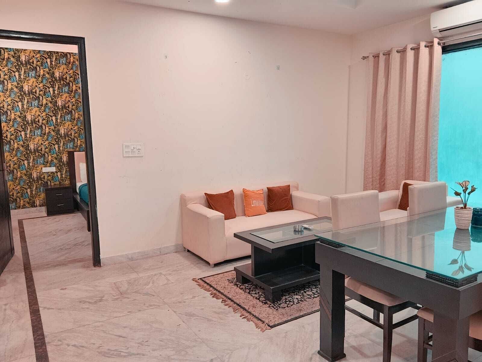 A modern living room with a glass dining table, white sofas, and a patterned wallpaper wall.
