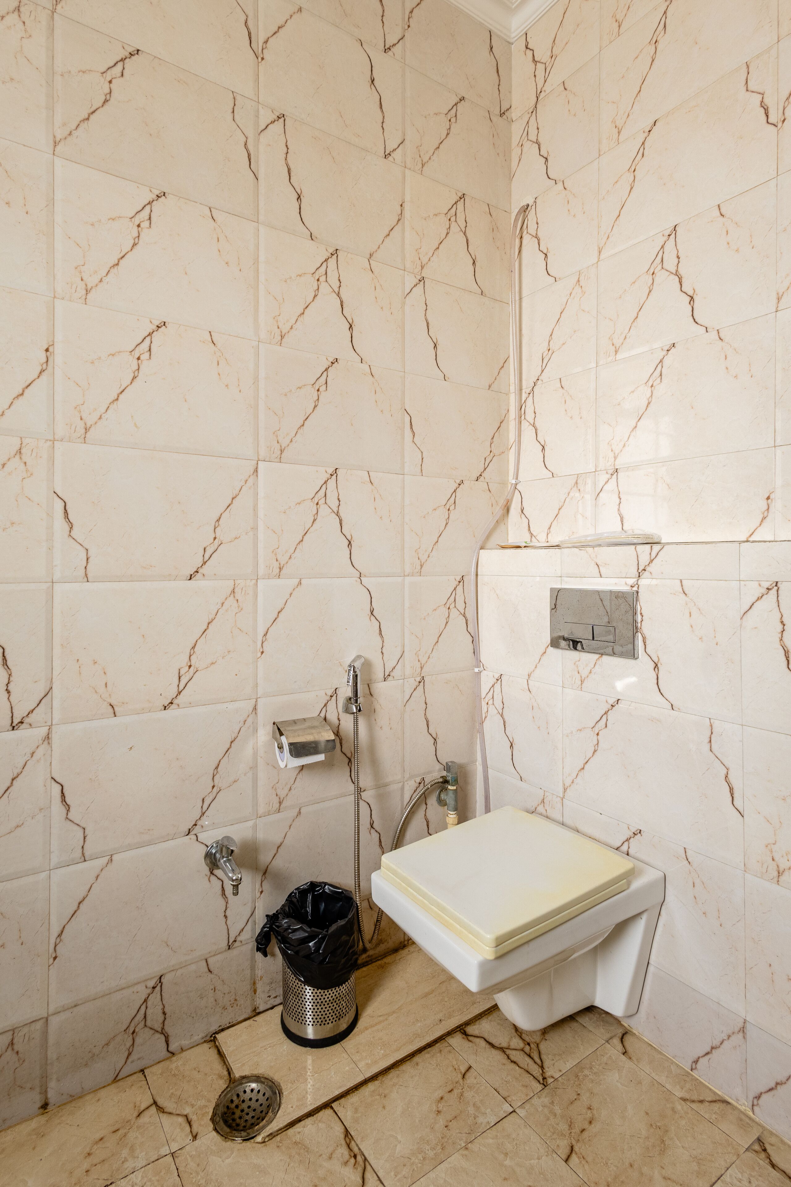 Une salle de bain avec des murs en marbre, des toilettes, un lavabo et une poubelle.