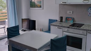 Et kompakt tekøkken med spiseplads, et fladskærms-tv og et maleri på væggen.