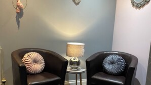 A room with two black leather armchairs, a small round table with a lamp, and decorative wall art. - Snaith Central Apartment (Goole)
