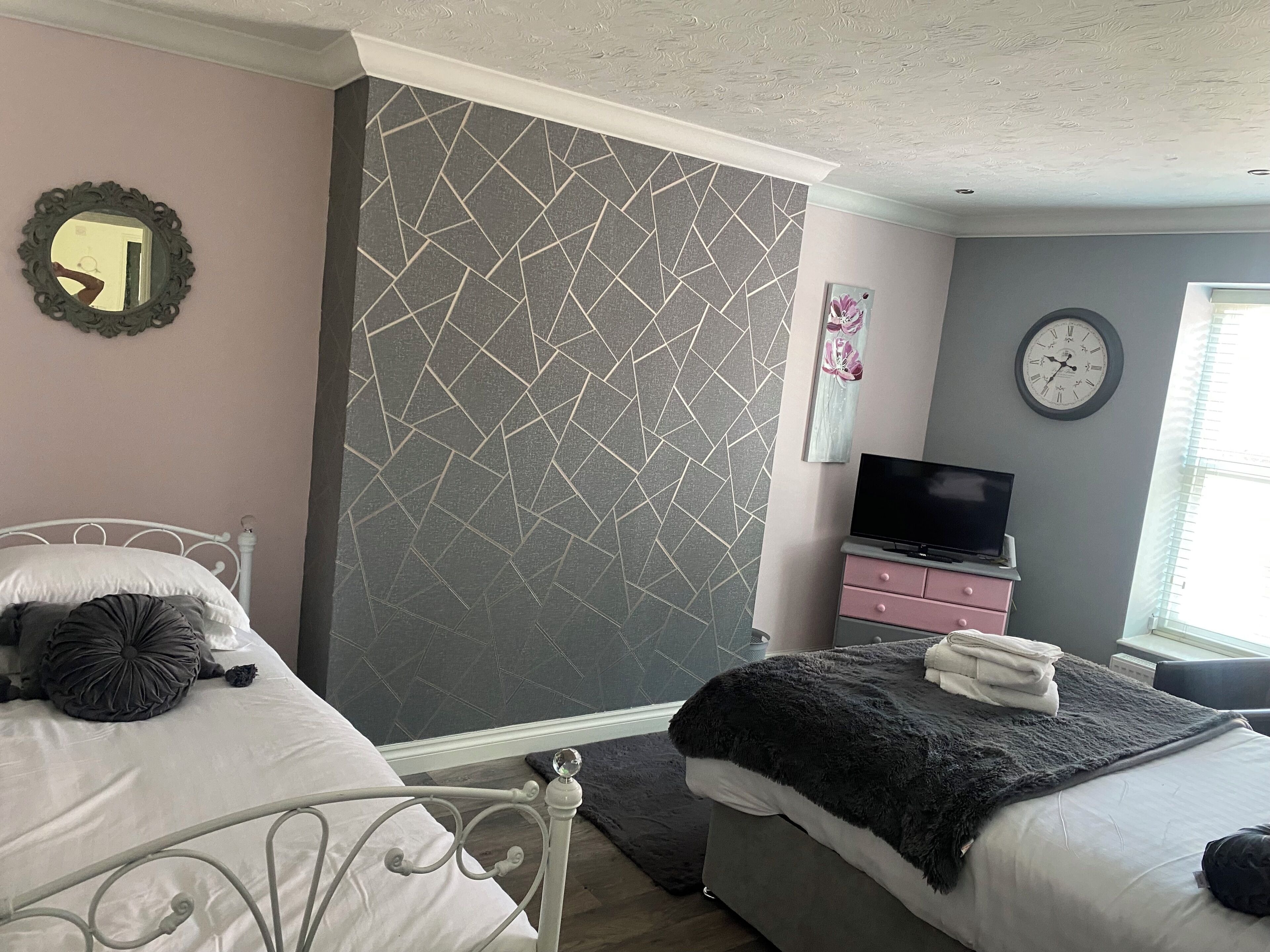 Une chambre avec deux lits, une télévision, une horloge et une fenêtre avec des stores.