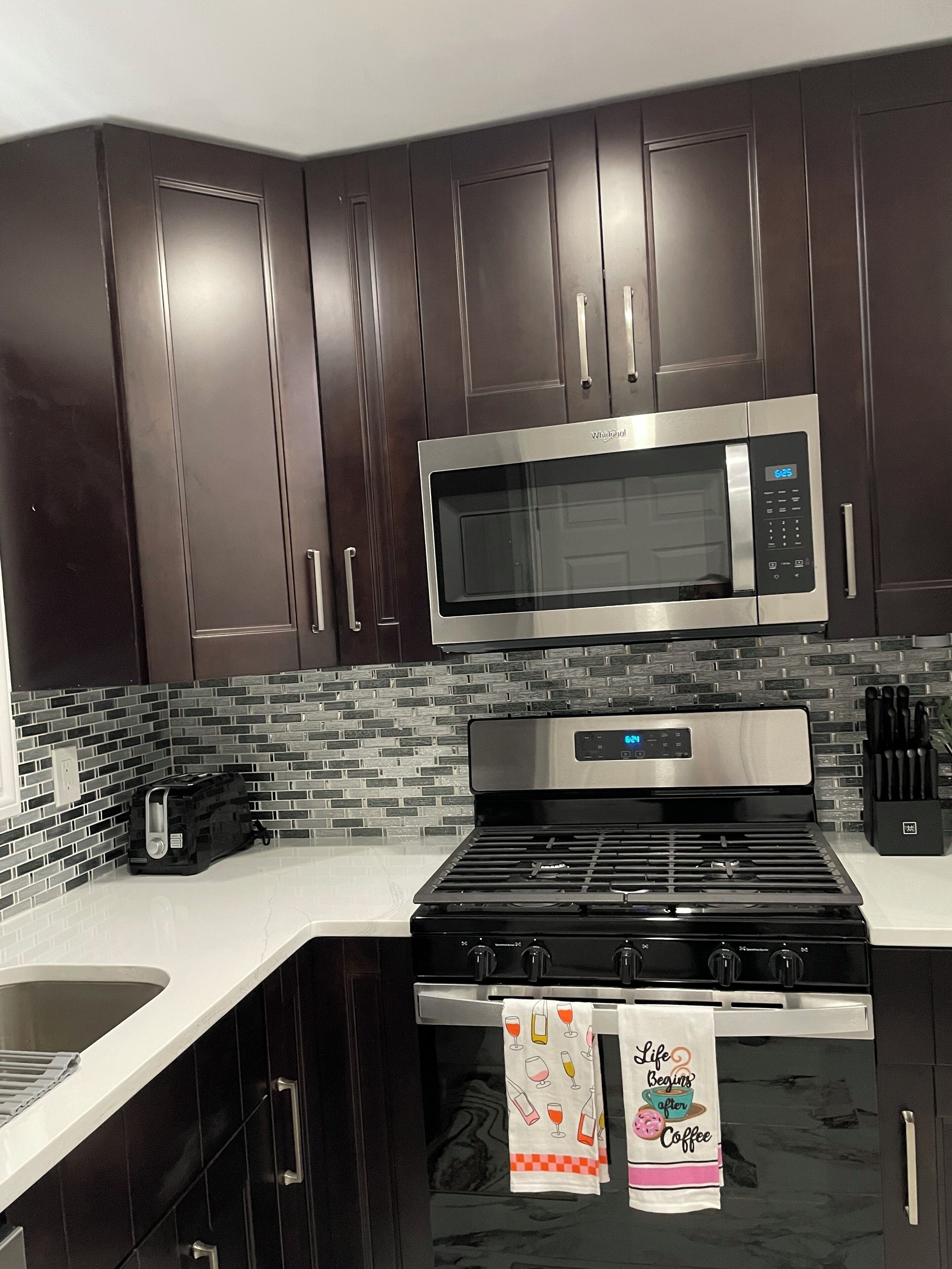 Uma cozinha moderna com armários escuros, micro-ondas de aço inoxidável, fogão a gás e painel de azulejos.