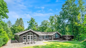 Eine Lodge mit einer großen Terrassenfläche, zahlreichen Fenstern und einem gepflegten Rasen.