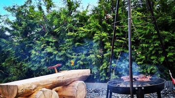 Ein Grillbereich im Freien mit Holz und Feuerstelle, umgeben von Kies und Grünpflanzen.