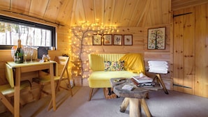A cozy cabin interior with a wooden ceiling, a yellow sofa, a dining table with chairs, and a small side table. - Sweet Donside Cabins (Strathdon)