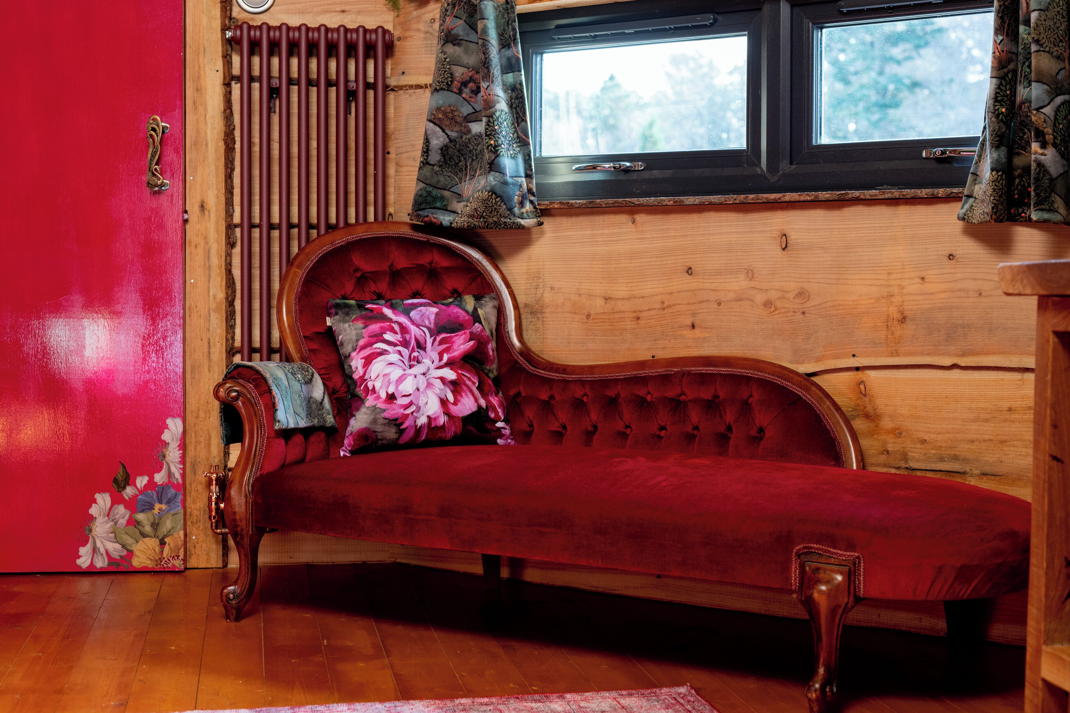 Un sofá rojo con un cojín estampado, un radiador de madera y una ventana con cortinas.