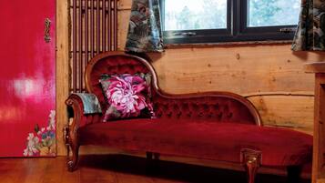 Un sofá rojo con un cojín estampado, un radiador de madera y una ventana con cortinas.