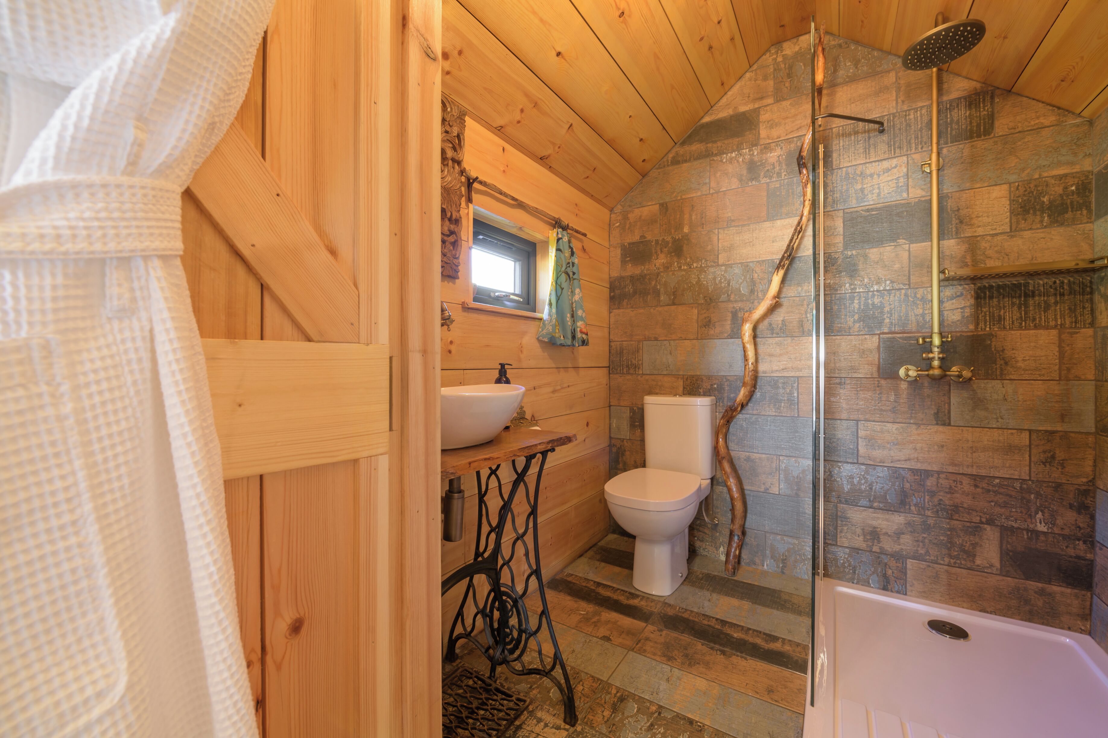 A wooden cabin bathroom with a shower, toilet, and sink.