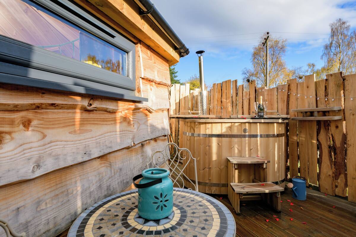 A wooden cabin with a hot tub, a small table, and a blue container.