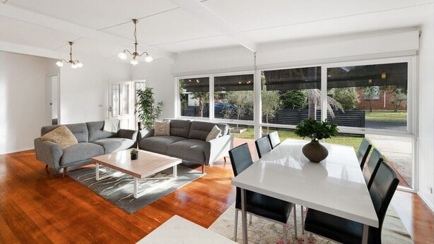 A spacious living room with a grey sofa, a coffee table, and a dining table with chairs. There are large windows providing a view of the outdoors. - Perfect location,  5 min walk to the beach, shops. Supermarkets and cafes.  (Cowes)
