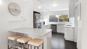 A modern kitchen with white cabinetry, a central island with bar stools, a stainless steel refrigerator, and a built-in oven. - Perfect location,  5 min walk to the beach, shops. Supermarkets and cafes.  (Cowes)